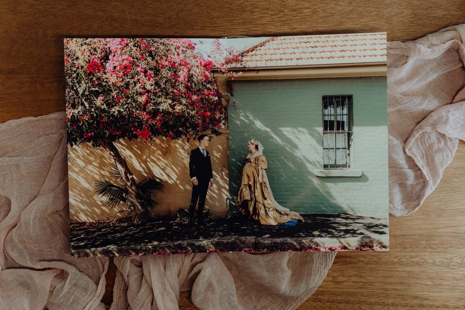 An open fine art album showing a couple by a green wall under bougainvillea
