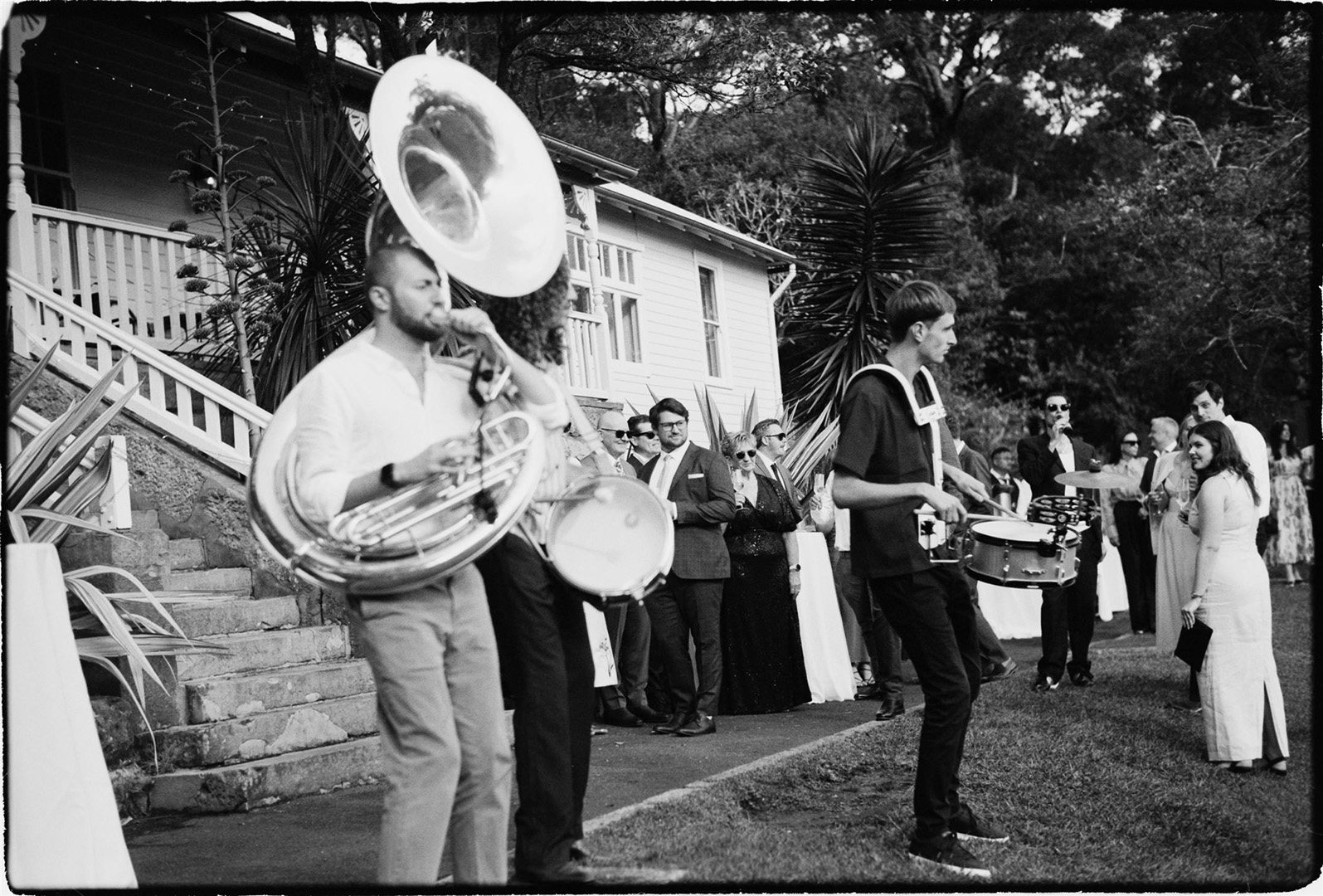 A brass band with a sousaphone playing as guests arrive at a garden wedding, a film frame