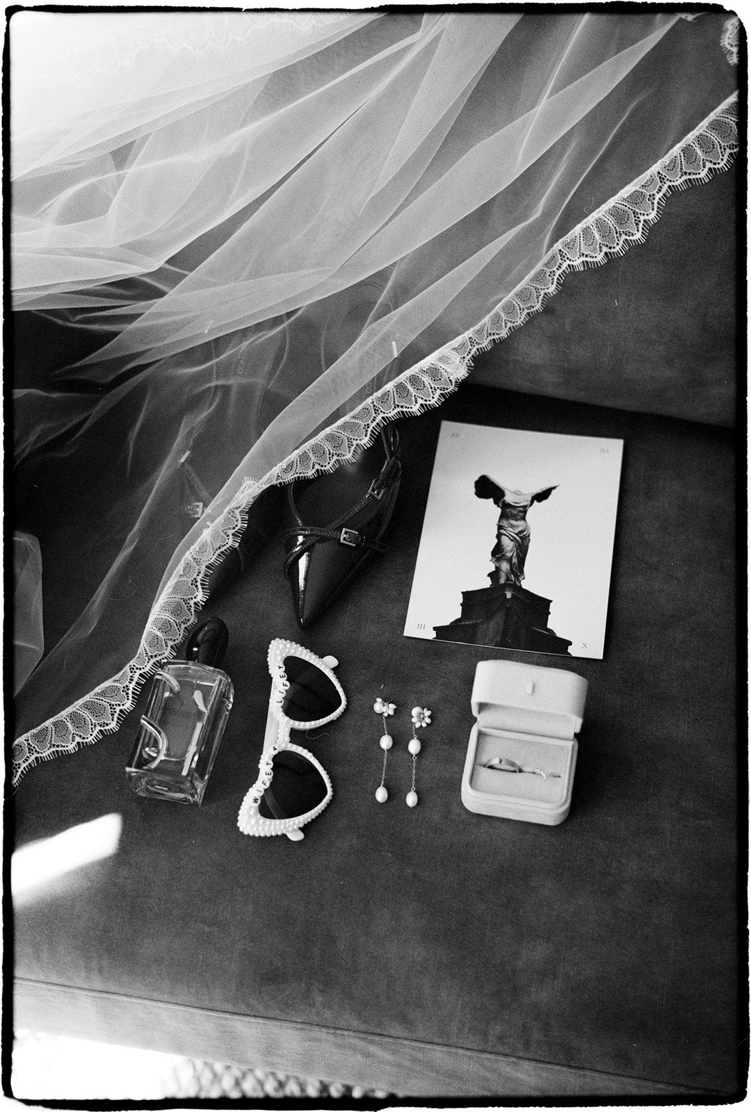 A veil, sunglasses and the invitation laid out on a table, a black and white film frame