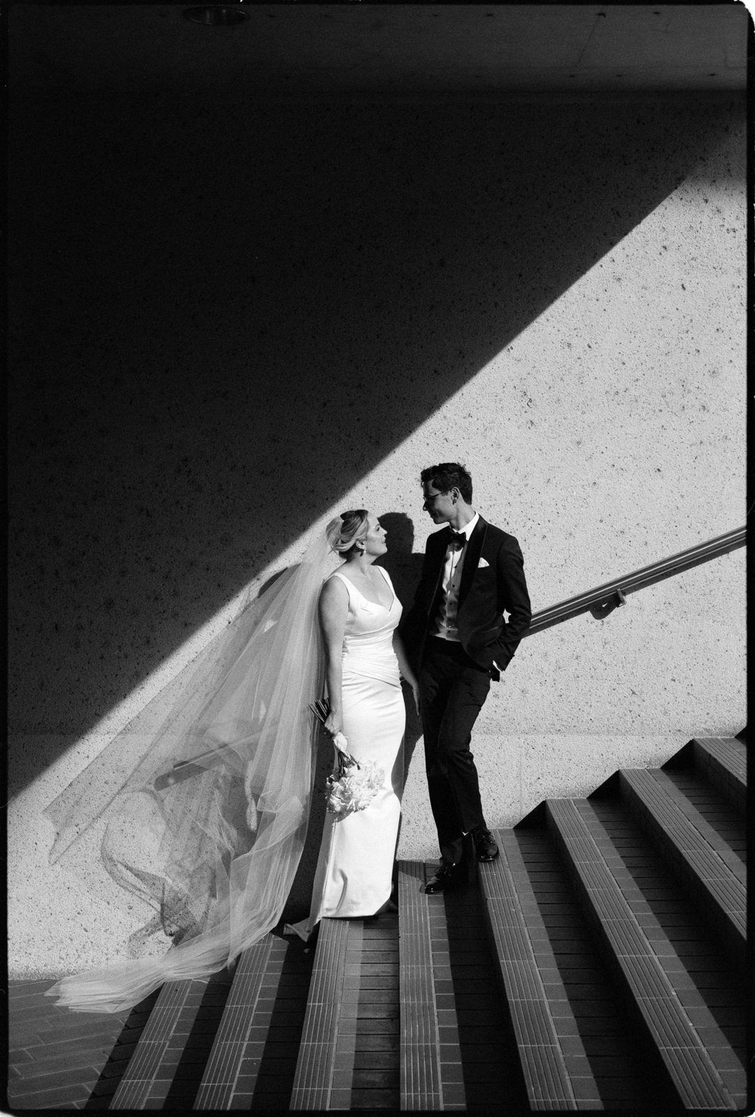 A couple walking down the Sydney Opera House stairs in hard sunlight, in black and white