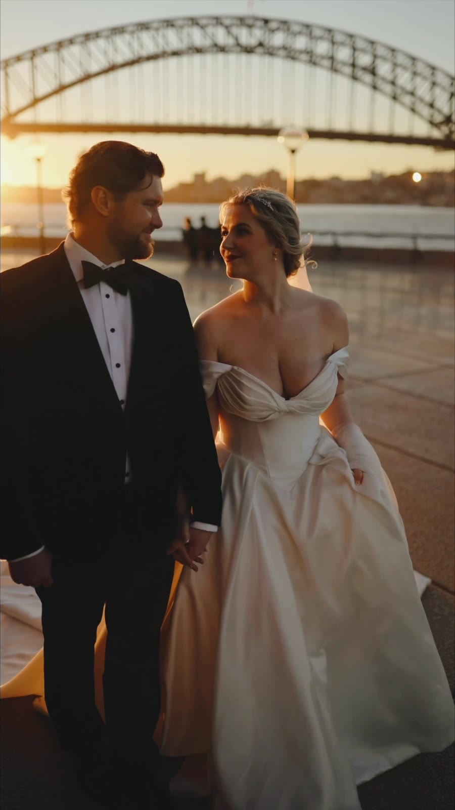 A couple walking at sunset by the Opera House with the Harbour Bridge behind them, a frame from their reel