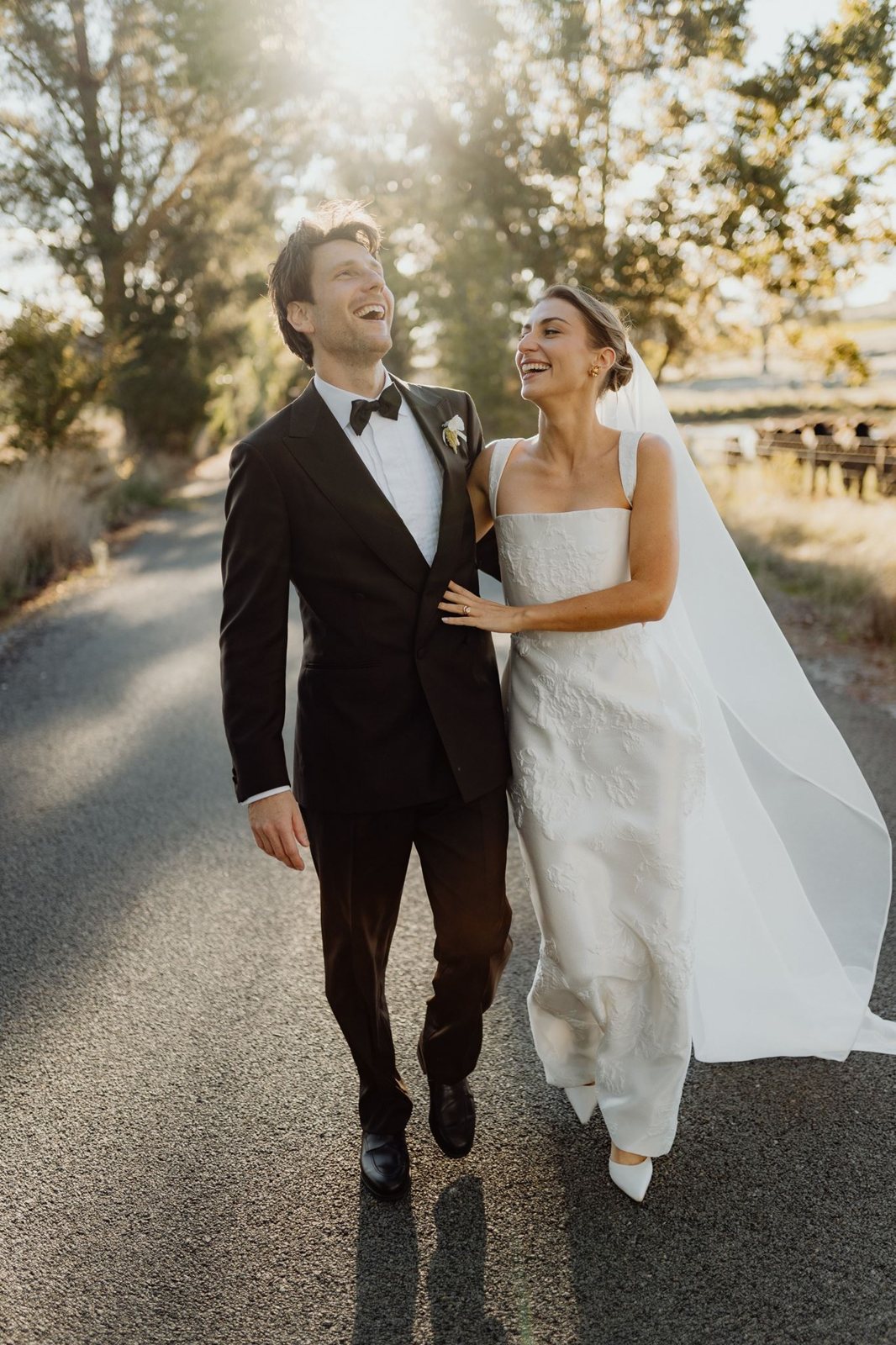 A bride and groom walking hand in hand down a path in golden sunset light