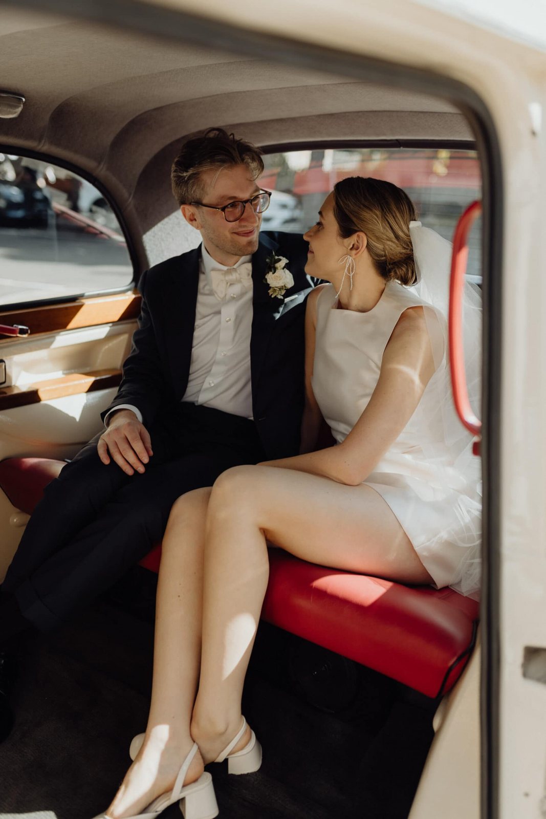 A bride and groom laughing in the back seat of a vintage car